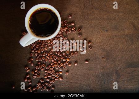 Tasse Kaffee und verstreute Kaffeebohnen auf dunkler Holzoberfläche Stockfoto