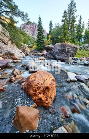 Großer roter Felsen im klaren, flachen Flussbett mit Berg in der Ferne Stockfoto