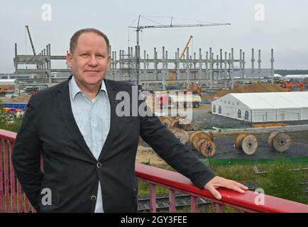 05. Oktober 2021, Brandenburg, Grünheide: Steffen Schorcht von der Bürgerinitiative Grünheide steht auf einer Brücke vor dem Rohbau der zukünftigen Batteriefabrik auf der Tesla Gigafactory Baustelle östlich von Berlin. Europas erste Tesla-Fabrik befindet sich auf der Zielgeraden. In Grünheide bei Berlin konnten die ersten E-Autos des US-Herstellers in wenigen Wochen vom Produktionsband Rollen. Das "Gigafactory" erschüttert nicht nur die europäische Automobilindustrie, es verursacht auch in der Region viele Unruhen. Foto: Patrick Pleul/dpa-Zentralbild/dpa Stockfoto