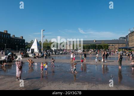 LONDON, GROSSBRITANNIEN - 08. Sep 2021: Viele Kinder und Eltern spielen in den Wasserfontänen von Coal Drops Yard, Kings Cross, London Stockfoto