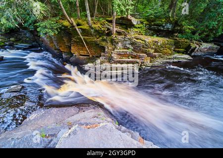 Kaskadierende Wasserfälle, die durch eine enge Schlucht mit einer Wand aus buntem moosigen Felsen führen Stockfoto