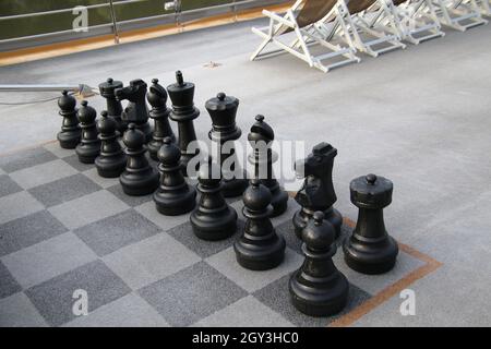 Große schwarze Schachfiguren im Freien, die draußen auf dem Boden auf einem gemusterten Schachbrett aufgestellt sind Stockfoto
