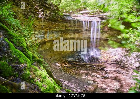 Wasserfall über einer kleinen Klippe neben einem moosigen Hügel Stockfoto
