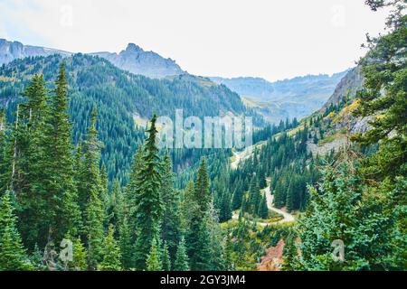 Unbefestigte Straße schlängelt sich durch das Tal der Bergketten mit Pinien gefüllt Stockfoto