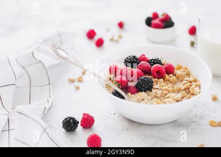 Morgens gesundes Frühstück, weiße Schale voll mit Müsli, Müsli, Himbeere, Brombeere auf grauem Betontisch. Gesunde Ernährung, Öko, Bio-Food-Konzept. Stockfoto