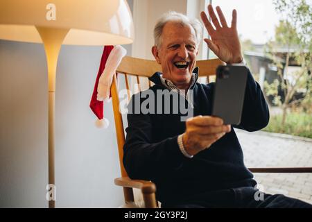 Glücklicher älterer Mann, der sich während eines Videoanrufs während der Weihnachtszeit mit seinen Angehörigen verbindet. Weihnachtsgrüße bei einem Videoanruf. Stockfoto
