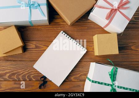 Draufsicht auf leeres Notizbuch und Geschenkboxen auf Holztisch Hintergrund. Weihnachtsneujahr und andere Feiertage Konzept. Platz für jedes Design kopieren. Raum für moderne kreative Arbeit eines Designers. Stockfoto