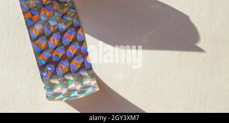 Ein Stück holographische Folie auf weißem Hintergrund, harte Schatten von der Folie. Draufsicht. Zu kopierende Position. Stockfoto