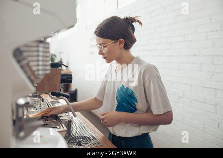 In der Cafeteria gibt es eine nette Barista, die die Kaffeemaschine putzt Stockfoto