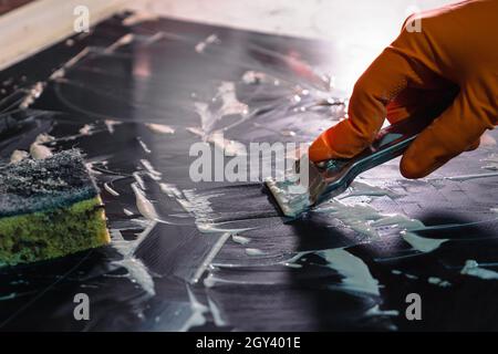 Orangefarbener Handschuh mit einem Metallschaber zum Reinigen des Kochfelds. Selektiver Fokus. Ein Schwamm liegt im Hintergrund. Das Konzept der Hausreinigung ein elektr Stockfoto