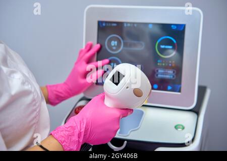 Eine Frau spielt eine Laser-Haarentfernungsmaschine. Sie hält einen funktionierenden Teil des Epilierers in ihren Händen und posiert für ein Foto. Es befindet sich in einem modernen Ba Stockfoto