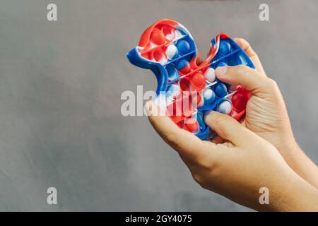 Anti-Stress-Spielzeug für Kinder einfaches Grübchen in Form einer Ente in den Händen einer Frau. Grauer Hintergrund. Nahaufnahme des popit-Spielzeugs Stockfoto