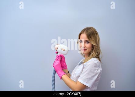 Eine Frau spielt eine Laser-Haarentfernungsmaschine. Sie hält einen funktionierenden Teil des Epilierers in ihren Händen und posiert für ein Foto. Es befindet sich in einem modernen Ba Stockfoto