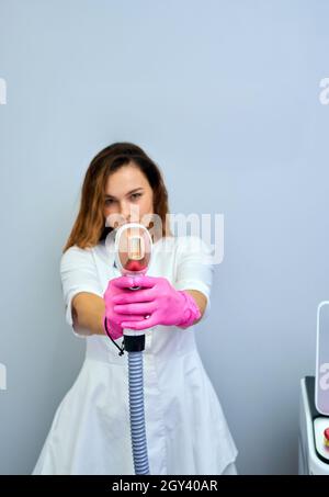 Eine Frau spielt eine Laser-Haarentfernungsmaschine. Sie hält einen funktionierenden Teil des Epilierers in ihren Händen und posiert für ein Foto. Es befindet sich in einem modernen Ba Stockfoto