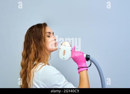 Eine Frau spielt eine Laser-Haarentfernungsmaschine. Sie hält einen funktionierenden Teil des Epilierers in ihren Händen und posiert für ein Foto. Es befindet sich in einem modernen Ba Stockfoto