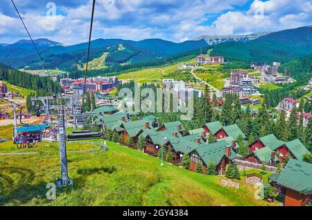 Die Fahrt mit dem Skilift über den steilen Hang des Berges Bukovel mit Blick auf das Tal mit Hotels, Hütten, Wäldern und Berglandschaften, Karpaten, Stockfoto