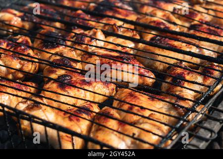 Gebratene Hähnchenflügel liegen auf einem Gitter auf der Holzkohle eines Holzkohlegrills. Selektiver Fokus. Das Konzept des Kochens im Hinterhof Stockfoto