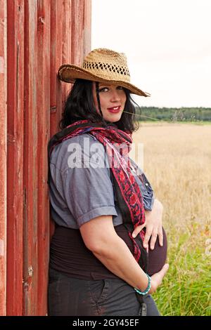 Umea, Norrland Schweden - 21. August 2021: Schwangere steht bei der roten Scheune Stockfoto