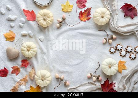 Weiße, natürliche Herbstdekorationen mit Platz zum Kopieren. Flach auf weißem Textil legen, Platz für Text. Kürbisse, trockene Blätter und Vogelbeeren, Sternkekse Stockfoto