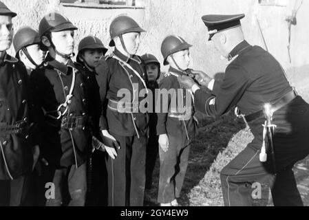 Ein Feuerwehrmann überprüft bei einer Übung der Kinderfeuerwehr ob Uniform eines Jungen richtig sitzt, Deutschland 1930er Jahre. Ein Feuerwehrmann ist die Überprüfung der rechte Sitz der Einheitlichen eines Jungen während eines Trainings der Junior Feuerwehrmänner, Deutschland 1930. Stockfoto