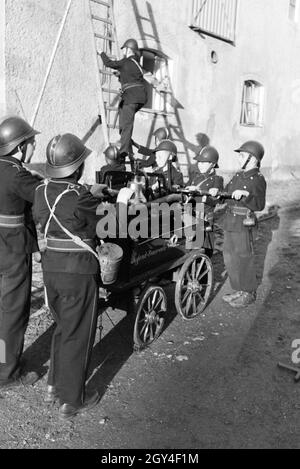 Eine Gruppe von der Kinderfeuerwehr mit dem Löschwagen und der Projektleiter bei einer Feuerwehrübung, Deutschland 1930er Jahre. Eine Gruppe von Junior Feuerwehrmänner ist die Vorbereitung der firewagon und Leiter während ein Feuerwehrmann, Deutschland 1930. Stockfoto