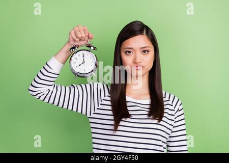 Portrait von attraktiven depressiven müde Mädchen in den Händen Uhr Wakeup isoliert über grüne Farbe Hintergrund halten Stockfoto