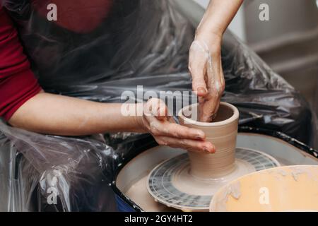 Nahaufnahme einer Frau, die auf dem Töpferrad einen Tonbecher formte. Potter Hände bilden Tonbecher spinnen auf Töpferscheibe auf Töpferwerkstatt Stockfoto