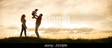 Kaukasische Familie, Mama, Papa und kleiner Sohn bei Sonnenuntergang. Silhouetten von Eltern und Kleinkind Junge auf dem Hintergrund des Himmels Freiheit und einen aktiven Lebensstil Stockfoto