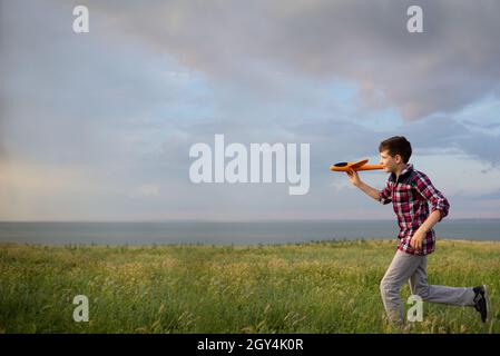 Der Junge rennt über das Feld und lässt ein Spielzeug-Flugzeug in den Himmel fliegen. Ein Kind, das vom Himmel träumt und im Sommer bei Sonnenuntergang in der Natur fliegt. Freiheit Stockfoto