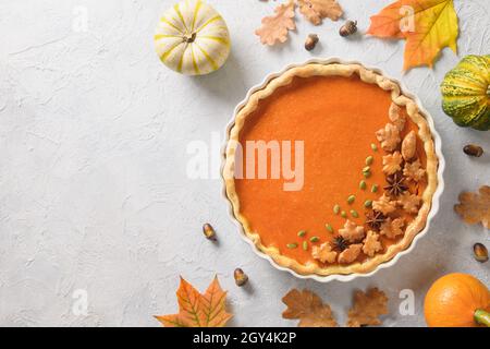 Hausgemachter, saisonaler, traditioneller amerikanischer Kürbiskuchen mit abfallenden Blättern auf hellem Hintergrund. Blick von oben. Festessen am Thanksgiving Day. Speicherplatz kopieren. Stockfoto