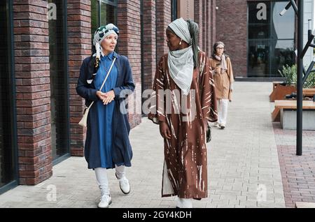 Muslimische Frauen in traditioneller Kleidung, die sich beim Spaziergang in der Stadt unterhalten Stockfoto