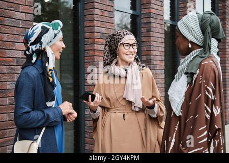 Glückliche muslimische Frauen in traditioneller Kleidung treffen sich in der Stadt, sie freuen sich, einander zu sehen Stockfoto