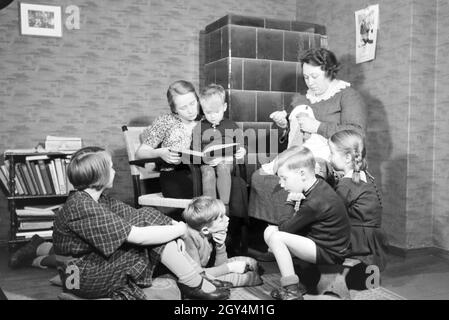 Mitglieder einer kinderreichen Familie lesen gemeinsam ein Buch, Deutsches Reich 30er Jahre. Mitglieder einer Großfamilie zusammen ein Buch lesen, Deutschland 1930. Stockfoto