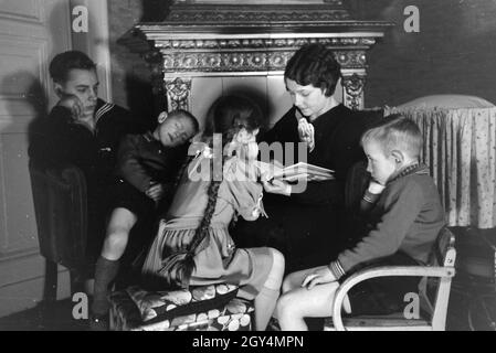 Mitglieder einer kinderreichen Familie lesen zusammen ein Buch, Deutsches Reich 30er Jahre. Mitglieder einer Großfamilie zusammen ein Buch lesen, Deutschland 1930. Stockfoto