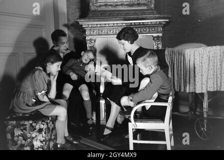 Mitglieder einer kinderreichen Familie lesen gemeinsam ein Buch, Deutsches Reich 30er Jahre. Mitglieder einer Großfamilie zusammen ein Buch lesen, Deutschland 1930. Stockfoto