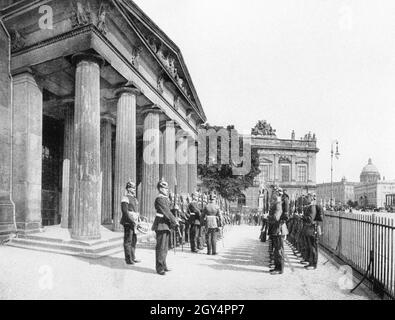 Zwei Wachen stehen sich vor dem Eingang zur Neuen Wache gegenüber und führen den Wachwechsel durch. Hinter ihnen sieht man das Zeughaus in Berlin-Mitte und das Berliner Schloss mit der Alten Kommandantur davor (rechts). Undatierte Fotografie, wahrscheinlich um 1900 aufgenommen. [Automatisierte Übersetzung] Stockfoto