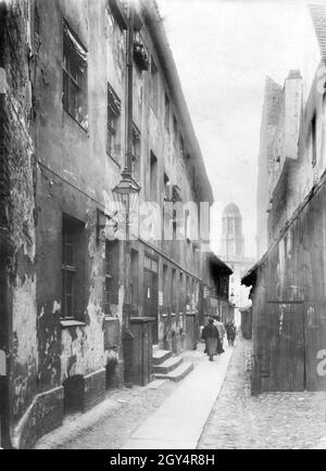 Passanten gehen 1925 durch eine Gasse, die zwischen Fischerbrücke und Fischerstraße auf der Fischerinsel in Berlin-Mitte verlief (Gasse gibt es heute nicht mehr). Im Hintergrund ist das Alte Rathaus (damals das Neue Stadthaus) zu sehen. [Automatisierte Übersetzung] Stockfoto