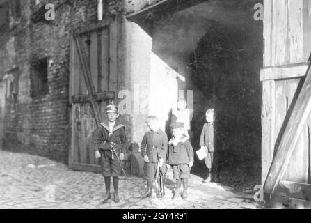 Fünf Kinder, vermutlich Geschwister, stehen 1907 in einem Hofeingang in der Gasse am Krögel in Berlin-Mitte, tragen Uniformen und tragen Spielzeugwaffen. [Automatisierte Übersetzung] Stockfoto