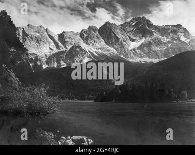 Das Zugspitzmassiv mit Waxenstein (links), Riffelsteinspitzen (Mitte) und Zugspitze (rechts) ist vom Ufer des Eibsee aus zu sehen. Das undatierte Foto aus dem Atelier von Rudolf Rudolphi aus Garmisch wurde vermutlich um 1925 aufgenommen. [Automatisierte Übersetzung] Stockfoto