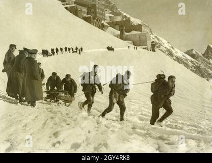 1934 fanden Übungen der Bergtruppen auf dem Zugspitzplatt statt. Auf dem Bild ist eine Säule vom Schneefernerhaus unterhalb des Zugspitzgipfens abgefahren und marschiert nun an ihren Offizieren entlang der verschneiten Hänge. Mehrere Soldaten auf einmal ziehen und schieben einen der Schlitten, die die notwendige Ausrüstung wie Ski tragen. Die Soldaten tragen Schneeschuhe. [Automatisierte Übersetzung] Stockfoto