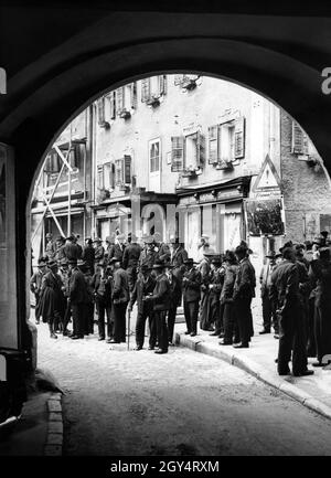 „nach dem Gottesdienst am Sonntagmorgen, dem 10. Mai 1937, treffen sich die Männer auf dem Marktplatz von Berchtesgaden zu einem Gespräch. In Haus Nr. 4 (Bildmitte) gibt es eine Konditorei und das Geschäft von Kathi Grüsser, die 'Delikatessen, Liköre, Reisevorräte' anbietet. Über dem Laden hängt ein Schild mit der Aufschrift „Nonntal und Hotel Bellevue“. An der Straßenecke hat der Bayerische Automobilclub ein Warnschild und einen Verkehrsspiegel für die Verkehrssicherheit angebracht. [Automatisierte Übersetzung]' Stockfoto