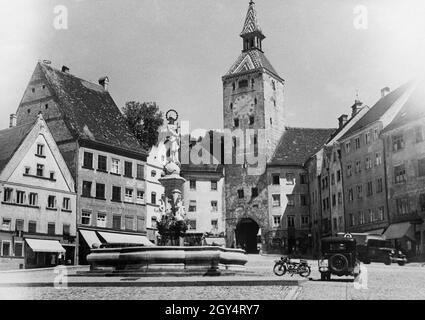 'In der Mitte des Hauptplatzes von Landsberg am Lech befindet sich der Marienbrunnen mit einer Marienstatue aus dem Jahr 1933. Dahinter bildet der Schmalzturm das Ende der mittelalterlichen, engeren Stadtmauer. Links im Haus Nr. 181 befindet sich das ''Kaufhaus Max Westheimer'', dessen gleichnamige jüdische Besitzerin 1938 auf Druck der Nationalsozialisten das Modehaus aufgeben musste und nach New York emigrierte. [Automatisierte Übersetzung]' Stockfoto