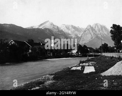 Das Foto zeigt Garmisch-Partenkirchen um 1900. Ein Herr mit Zylinderhut steht am Ufer der Loisach vor der Brücke der Fürstenstraße. In der Mitte des Bildes ist der Kirchturm der Pfarrkirche St. Martin zu sehen. Im Hintergrund erhebt sich das Zugspitzmassiv mit (von links nach rechts): Alpspitze, Höllentalspitzen, Waxenstein, Zugspitze. Foto aus dem Kunstverlag von Max Stuffler aus München. [Automatisierte Übersetzung] Stockfoto