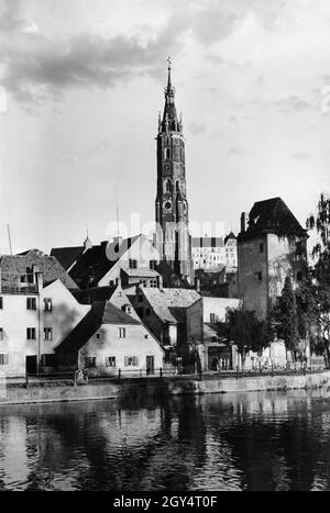 Der Blick geht vom Sausteg über die Isar zur Isarpromenade in der Altstadt von Landshut. Dort steht der Obere Länd-Turm (oder Röcklturm), der Teil der alten Stadtbefestigung war. Dahinter erhebt sich der Turm der St. Martins-Kirche, der einen Teil der Burg Trausnitz verbirgt (dahinter rechts). Das undatierte Foto wurde wahrscheinlich in den 1930er Jahren aufgenommen. [Automatisierte Übersetzung] Stockfoto