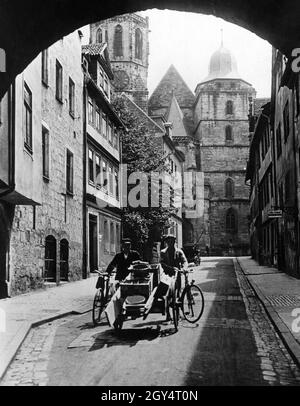 Der Durchgang unter dem Münzmeisterhaus in Coburg führt in die Neugasse und bietet einen Blick auf die Stadtkirche St. Moriz mit ihrem unvollendeten Südturm. Zwei Arbeiter gehen an einem späten Morgen im Jahr 1931 mit zwei Rädern und einem Handwagen durch die Gasse in Richtung des Durchgangs. Sie haben Eimer und Bretter geladen. Auf der rechten Seite befindet sich ein Geschäft von Julius Pechauf. [Automatisierte Übersetzung] Stockfoto