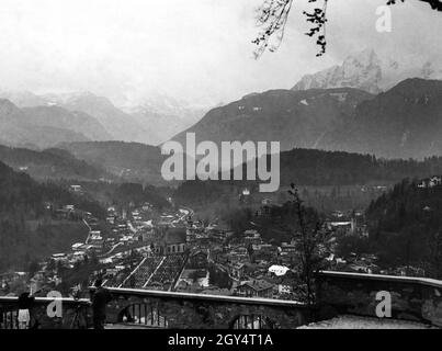 Der Blick geht vom Lockstein über Berchtesgaden mit dem Friedhof am Franziskanerkloster und der Evangelisch-Lutherischen Christuskirche (rechts) Richtung Königssee und Watzmann (rechts). Ein anderer Fotograf steht auf dem Lockstein mit seiner Kamera auf einem Stativ. [Automatisierte Übersetzung] Stockfoto