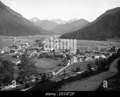 Der Blick geht über Mittenwald mit der Pfarrkirche St. Peter und Paul im Zentrum in Richtung Tiroler Berge bei Seefeld im Süden. [Automatisierte Übersetzung] Stockfoto
