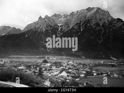 Dieses Foto, aufgenommen um 1910, zeigt Mittenwald mit der Kirche St. Peter und Paul in der Mitte und St. Nikolaus auf der linken Seite. Hinter dem Dorf erhebt sich das nördliche Karwendelgebirge mit Karwendelkopf, Karwendelspitze und Linderspitze. Foto aus dem Kunstverlag von Max Stuffler aus München. [Automatisierte Übersetzung] Stockfoto