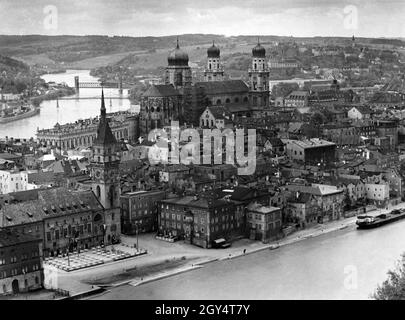 Der Blick aus dem Jahr 1937 von der Veste Oberhaus ist auf die Halbinsel zwischen Donau (rechts) und Inn (links), auf der die Altstadt von Passau liegt. Der Fünferlsteg zur Kirche St. Severin (ganz links) und die Kaiserin-Elisabeth-Brücke für die Eisenbahn führen über den Inn. In der Altstadt steht der Rathausturm am alten Rathaus (vorne links), vor dem Tische für eine Party aufgestellt wurden. Am Stephansdom (Bildmitte) befindet sich ein Holzgerüst für Renovierungsarbeiten. [Automatisierte Übersetzung] Stockfoto