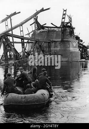 Deutsche Wehrmachtssoldaten sitzen in einem Schlauchboot und überfliegen eine gesprengte Brücke. [Automatisierte Übersetzung] Stockfoto